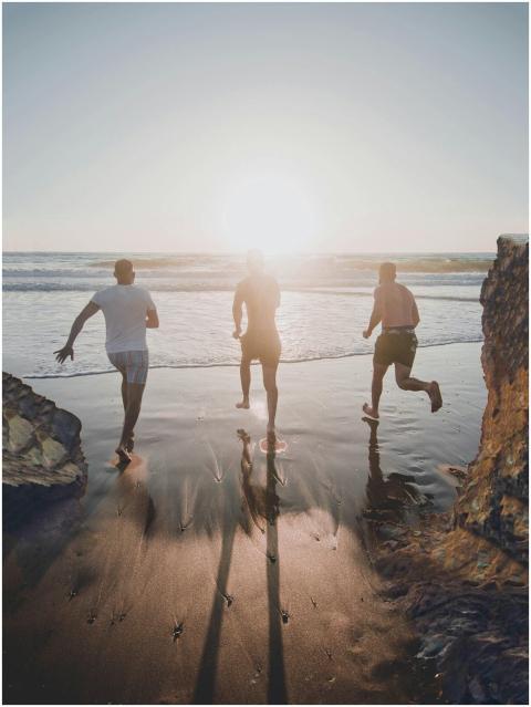 Three men run joyfully towards the ocean at sunset