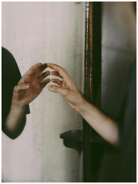 A person's hand reaching towards its reflection in