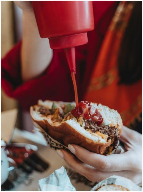 Crop faceless woman in red clothes adding ketchup