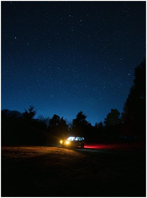 A car with headlights on, parked on a dark forest
