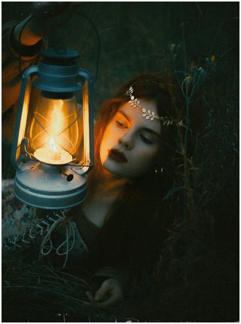 A woman holding a vintage lantern in a dark, moody