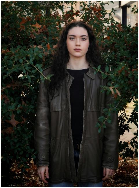 A woman with curly hair in a leather jacket stands