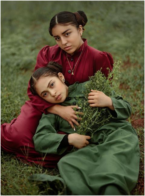 Two sisters in vibrant dresses share a tender mome