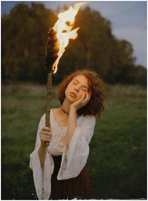 A woman in vintage clothing holds a torch outdoors
