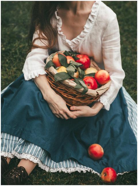 A woman in vintage dress holding a basket of apple