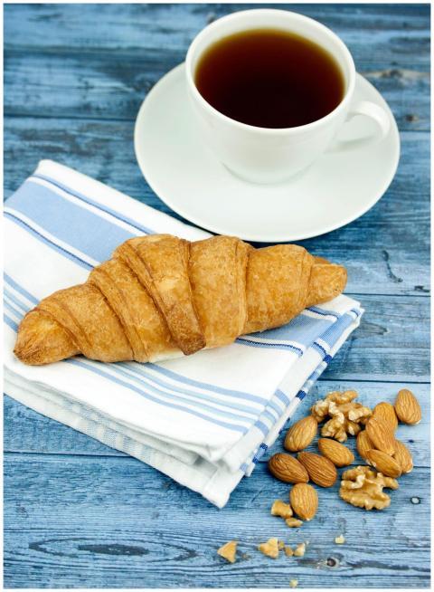 A warm croissant with black coffee and nuts on a r
