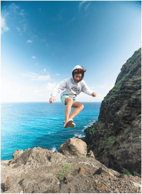 Person jumping off a cliffside by the ocean in Wai