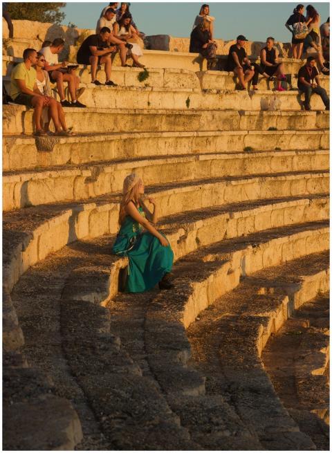 Woman in turquoise dress seated in ancient amphith