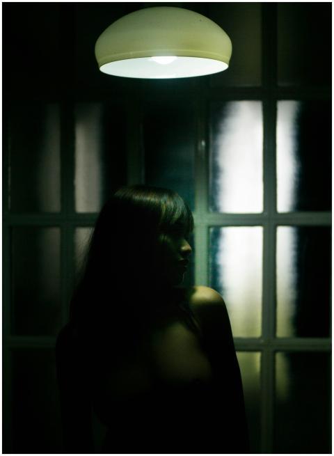 Emotionless brunette standing in shadows under dim