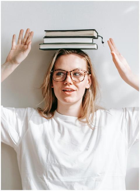 Sincere young female in eyewear and pile of textbo