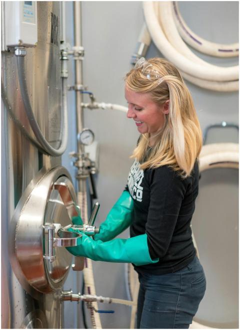 Female brewery worker in safety gear operating bre