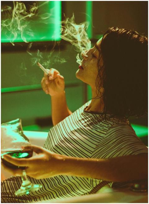 A woman enjoys a cigarette and wine in a cozy, neo