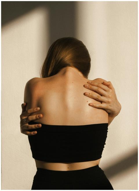 A woman in a black tube top embraces herself, crea