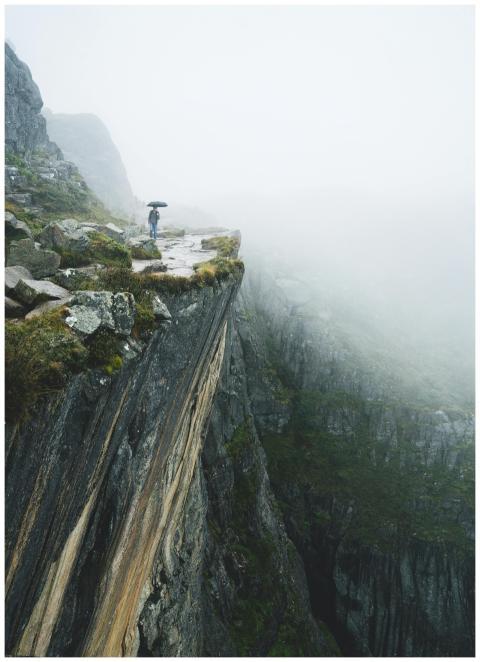 A person with an umbrella stands on a foggy mounta