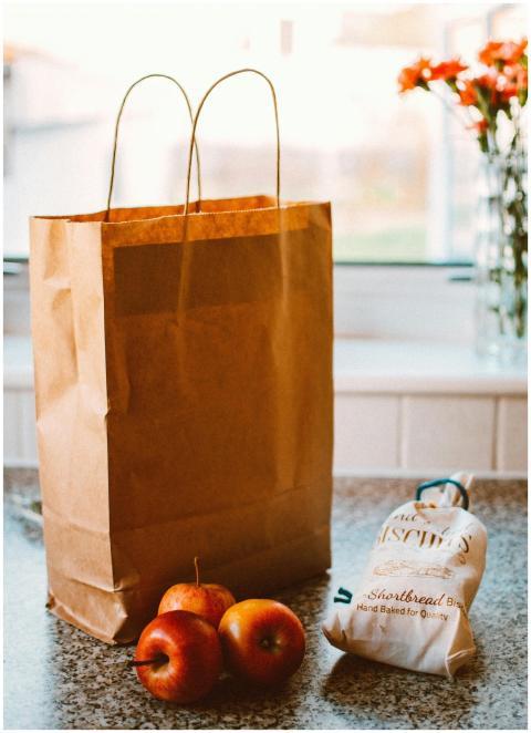 A paper bag with apples and packaged goods on a ki