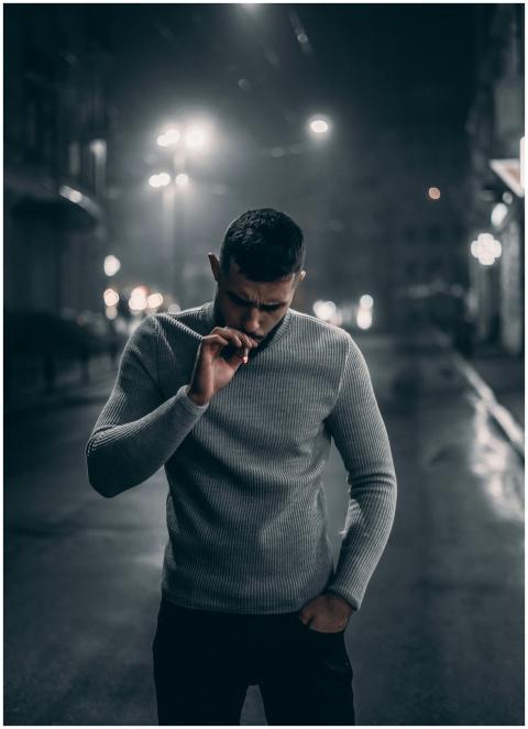 A fashionable man in a sweater smokes in a city st