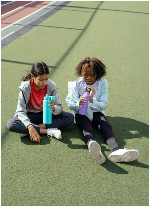 Two young girls sit on a sports ground enjoying a