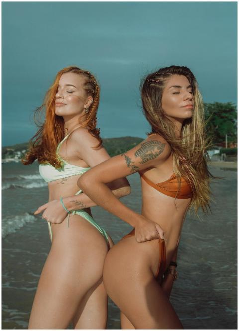 Two women posing confidently in swimsuits by the b
