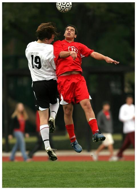 Two soccer players in mid-air challenge on a green