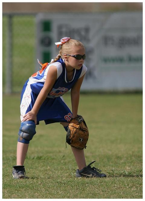 A young girl in a softball uniform and sunglasses