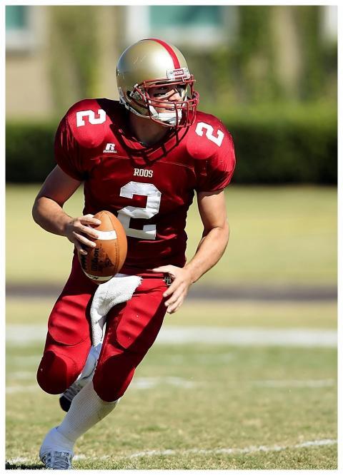 Quarterback in red jersey running with football on