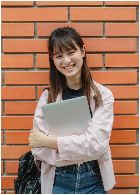 Cheerful Asian student holding a laptop, smiling a