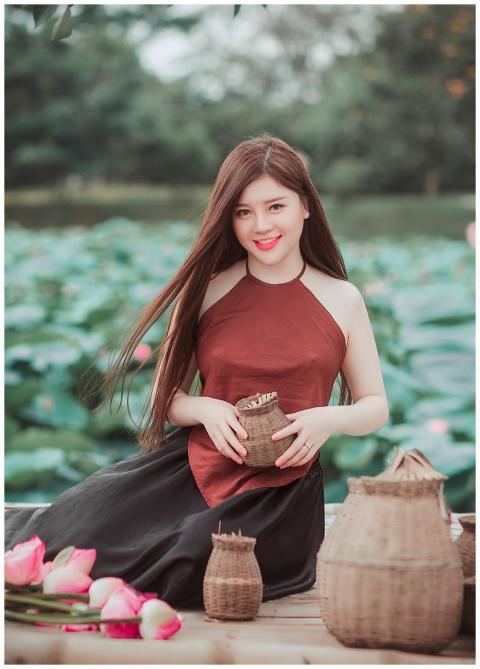 An Asian woman sits with baskets among lotus flowe