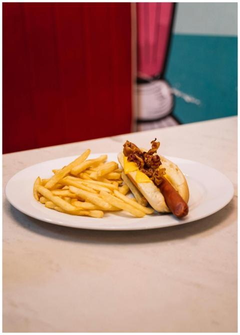 Close-up of a hotdog with cheese and fries on a wh