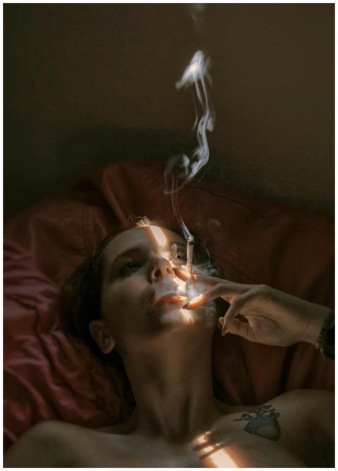 A woman lying on a bed indoors, smoking a cigarett