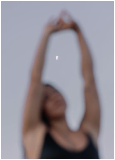 A woman stretches with arms raised, silhouetted ag