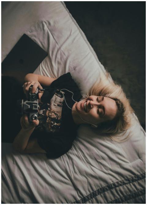 Woman lying on bed, smiling while using a game con