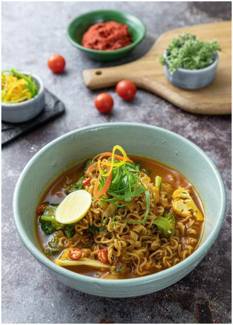 A vibrant bowl of spicy Asian noodle soup garnishe