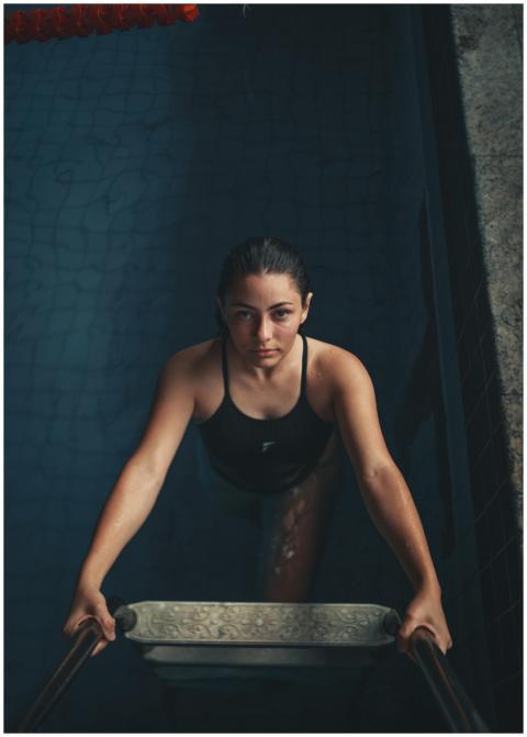 Young woman in a black swimsuit climbing a pool la