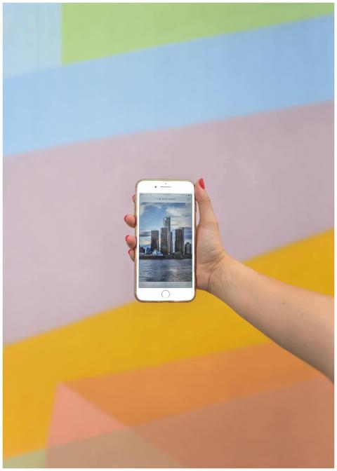 A hand holds a smartphone displaying a Detroit sce