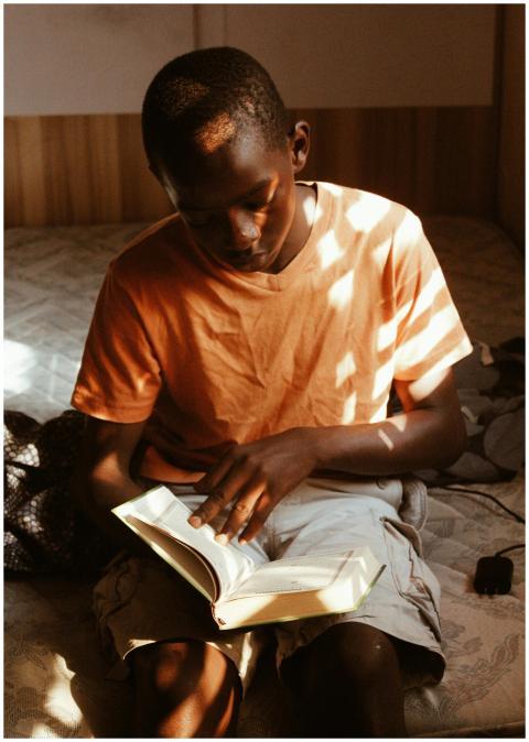 A young boy reading a book in a sunlit room with l