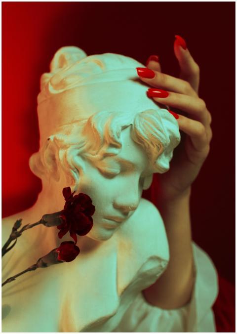 A marble bust elegantly touched by hands with red