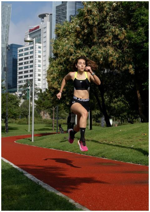 Fit woman running on red track in city park, build