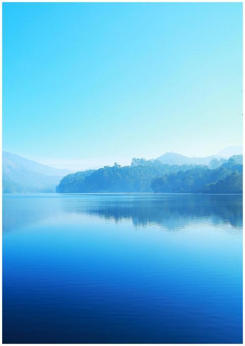 A tranquil lake reflecting misty mountains under a