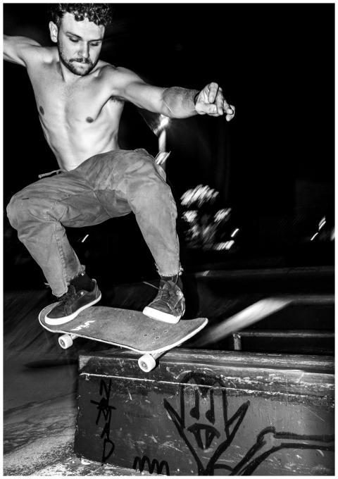 Shirtless skateboarder performs a trick at night i