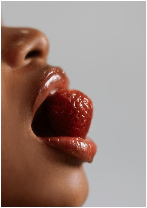 Artistic close-up of lips holding a strawberry, em