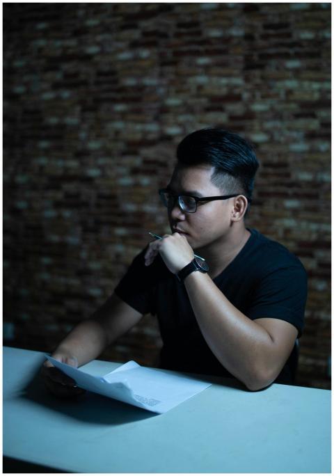 Man wearing glasses thinking with a pen at a table