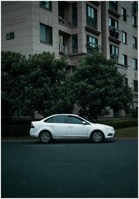 White sedan parked on road beside apartment buildi