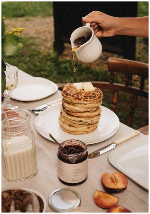 Stack of pancakes with syrup being poured, surroun