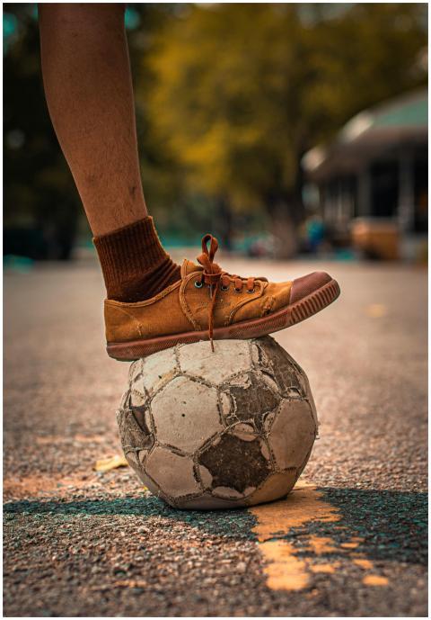 An aged soccer ball under a foot in casual footwea