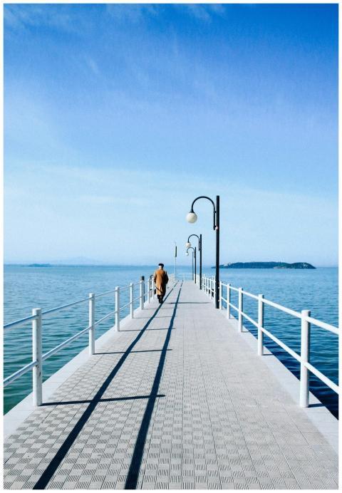 A lone figure walks along a pier extending into th