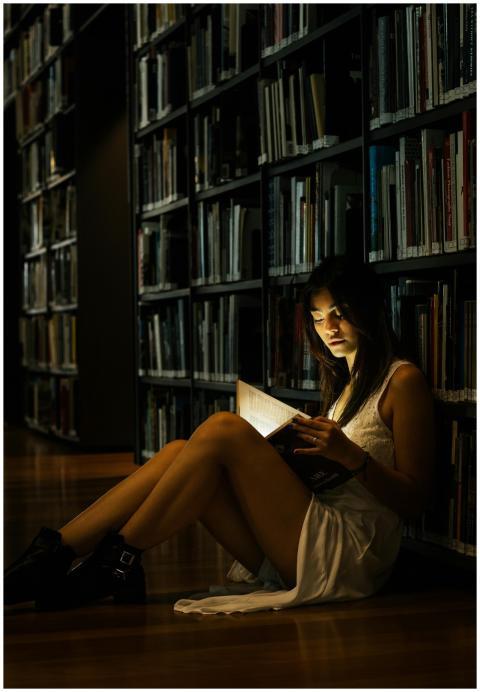 A woman reads a glowing book on the floor of a dim