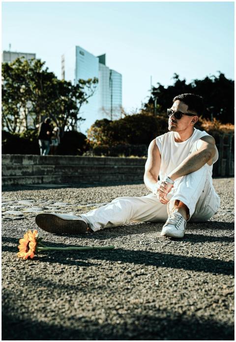 Casual young man sits on park path with a sunflowe