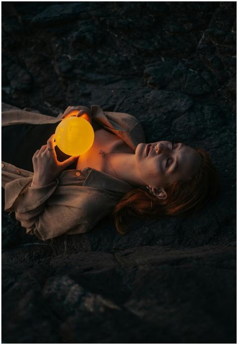 A woman lies on rocks in darkness, holding a glowi