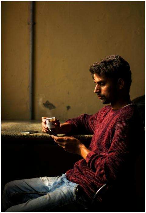 A young man in a maroon sweater sits indoors, hold