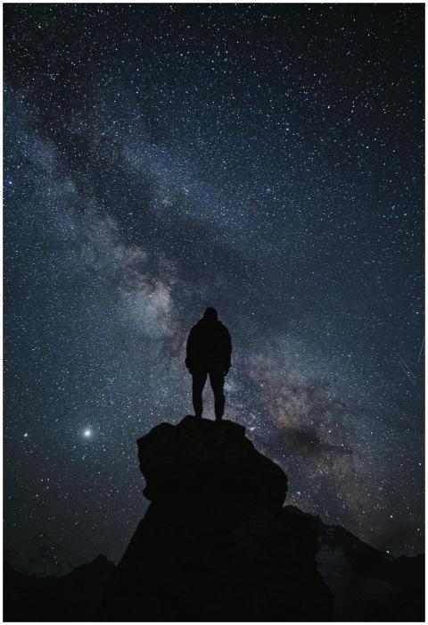 Person silhouette standing on rock under a vast st